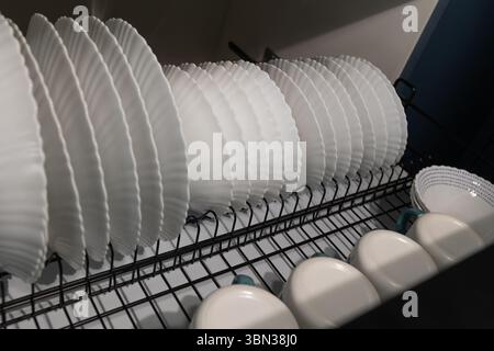 La vaisselle propre est soigneusement disposée dans une grille, séchant après avoir été lavée. La cuisine présente un design contemporain avec des assiettes et des tasses blanches de manière organisée. Banque D'Images