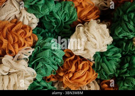 Éponges de bain en maille colorées dans des tons orange, vert et blanc empilées dans un affichage pour une utilisation dans la salle de bain et les routines de soin de la peau Banque D'Images