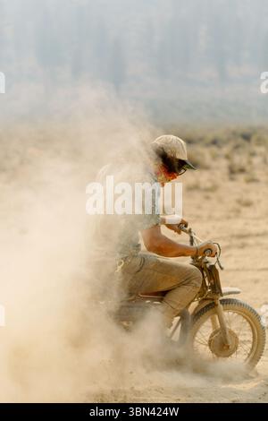 Motocycliste roulant sur un chemin de terre donnant un coup de pied vers le haut du nuage de poussière Banque D'Images