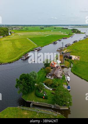 Une vue aérienne pittoresque d'un moulin à vent hollandais à côté d'un canal avec des bateaux, entouré de champs verdoyants, de maisons traditionnelles, et de voies navigables lointaines un Banque D'Images