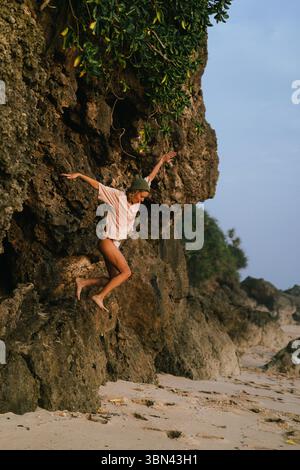 Femme ludique sautant des rochers de plage avec les bras tendus Banque D'Images