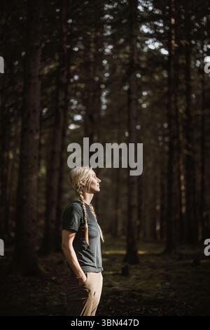 Belle femme blonde au look serein se dresse au milieu de la forêt Banque D'Images