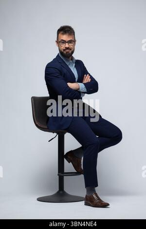 Homme espagnol en costume bleu assis sur le tabouret avec les bras croisés Banque D'Images