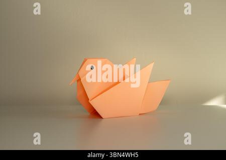 Figurine d'oiseau en papier pliée à partir de papier couleur pêche sur un fond clair Banque D'Images
