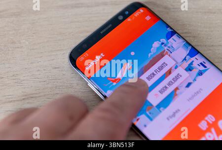 Londres. UK- 06.27.2025. Un téléphone portable avec l'application Easyjet à l'écran et une personne appuyant sur l'icône réserver des vols. Banque D'Images