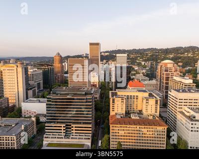 Vue aérienne en hauteur sur une rue centrale du centre-ville de Portland, avec la ligne d'horizon de la ville et les collines vertes au loin au coucher du soleil, Oregon Banque D'Images