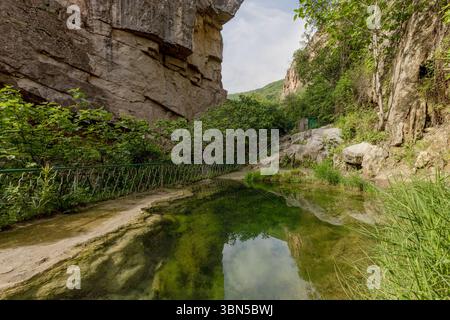 Pont du diable, une arche naturelle en travertin enjambant la profonde rivière Vorotan. Ci-dessous, des sources minérales chaudes créent des stalactites colorées dans des grottes cachées. Banque D'Images