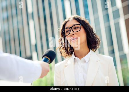 Jeune femme professionnelle interviewée à l'extérieur dans un paysage urbain moderne au cours d'une journée lumineuse et ensoleillée Banque D'Images