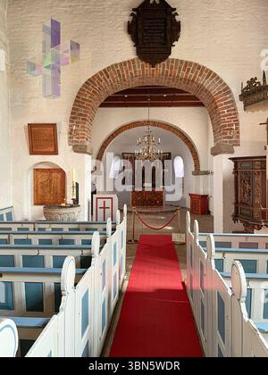 Sylt, Deutschland 14. Mai 2025 : Im Bild : Ein eindrucksvoller Blick in das Innere der über 800 Jahre alten Evangelisch-Lutherischen est Martin Kirche in Morsum auf Sylt. DAS Bild zeigt das historische Kirchenschiff mit seinen Weiß getünchten Wänden und den markanten Rundbögen aus rotem Backstein, die den Weg zum Altarraum weisen. IM Vordergrund sind die traditionellen, blau-Weiß gestrichenen Kirchenbänke zu sehen, die einen roten Teppich flankieren, der den Mittelgang ziert. An der linken Seite ist das historische Taufbecken mit einer großen Kerze zu erkennen, während an der rechten Seite die R Banque D'Images