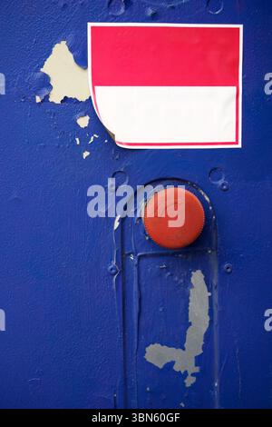 Bouton-poussoir d'urgence avec autocollant blanc et rouge vierge sur la surface bleue usée. Banque D'Images