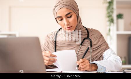 Jeune femme médecin concentrée dans hijab prendre des notes en clinique Banque D'Images
