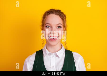 Jeune étudiant excité exprimant la joie devant un fond jaune vif portant un gilet vert élégant et une chemise blanche Banque D'Images