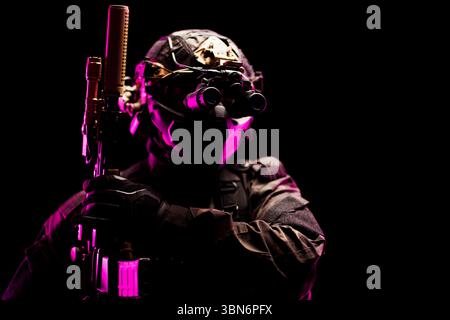 Un opérateur tactique équipé d'un équipement de vision nocturne avancé et d'un uniforme de protection sous un éclairage rose spectaculaire. Banque D'Images