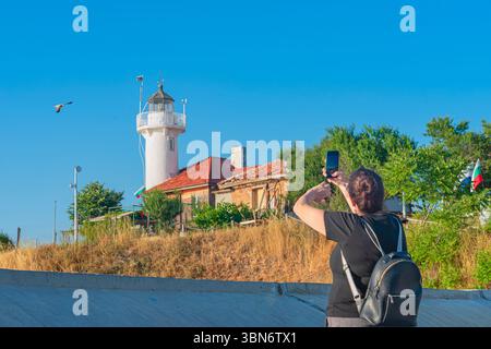 Femme touriste avec sac à dos prend la photo du phare blanc et de la vieille maison sous ciel bleu clair le jour ensoleillé. Concept de beauté phare, tourisme Banque D'Images