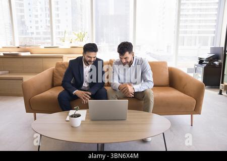 Deux jeunes hommes d'affaires heureux regardent la présentation vidéo sur l'écran d'ordinateur portable Banque D'Images