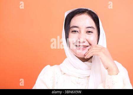 Une belle jeune femme musulmane souriante portant un hijab, regardant directement la caméra avec une expression douce. L'image capte sa sérénité et sa joie Banque D'Images