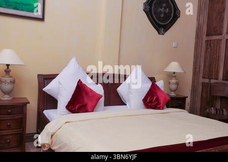 Cette chambre accueillante est agrémentée d'un cadre de lit classique en bois, d'une literie d'un blanc éclatant et d'oreillers marron décoratifs, le tout agrémenté d'une finition murale chaleureuse et texturée. A Banque D'Images