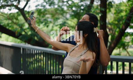 Jeune couple s'amusant, enregistrant une vidéo de danse ludique avec smartphone dans un parc Banque D'Images