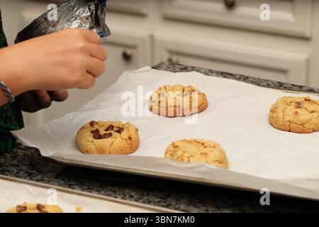 Un boulanger ajoute des pépites de chocolat sur des biscuits chauds fraîchement cuits Banque D'Images