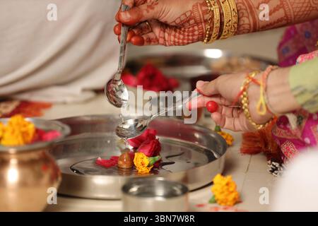 Gros plan d'un rituel de mariage hindou impliquant une offrande d'eau sacrée (Abhishekam ou Achamanam). Deux mains (un mâle, une femelle) tenant des cuillères Banque D'Images