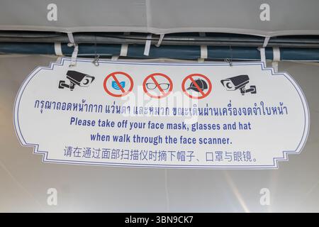 Un panneau indique aux gens d'enlever les masques faciaux, les lunettes et les chapeaux avant de marcher à travers un scanner de visage, en trois langues, Musée national de Bangkok Banque D'Images