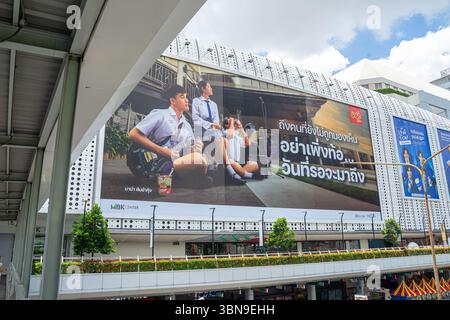 Un grand panneau publicitaire de nouilles instantanées thaïlandaises représentant des jeunes en uniforme, est apposé sur le côté d'un bâtiment moderne près d'une passerelle Banque D'Images