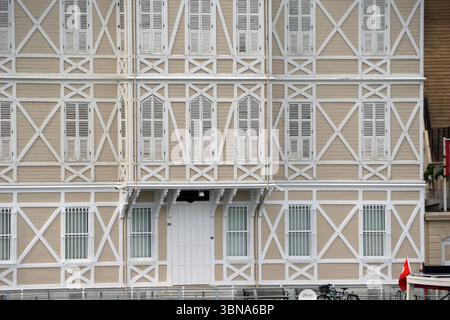 Istanbul, Turquie. La plus grande ville de Turquie et l'une des rares villes transcontinentales au monde, couvrant à la fois l'Europe et l'Asie à travers le détroit du Bosphore., Un bâtiment de trois étages avec une façade beige clair ou crème et des poutres en bois blanc et des supports. Le bâtiment dispose de plusieurs fenêtres avec des volets blancs, dont certains sont fermés. Une porte blanche est située au rez-de-chaussée, flanquée de deux fenêtres de chaque côté. Le bâtiment a un toit légèrement incliné, et une petite partie d'un drapeau rouge est visible sur le côté droit de l'image. Un vélo est garé devant le Banque D'Images