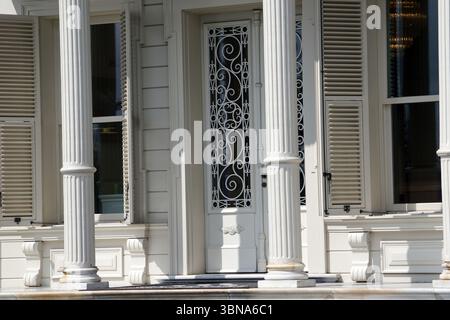 Une maison blanche avec une porte d'entrée blanche ornée d'une grille décorative en métal. La maison a des colonnes blanches et des volets de chaque côté de la porte, et les volets sont partiellement ouverts. La maison est située sur un porche en pierre de couleur claire ou en béton, et une partie d'une deuxième fenêtre est visible à gauche de la porte principale. L'extérieur de la maison est principalement blanc, avec certaines zones montrant une couleur crème ou blanc cassé. Légende façonnée par l'œil d'un artiste et l'imagination. Istanbul, Turquie. La plus grande ville de Turquie et l'une des rares villes transcontinentales au monde, couvrant à la fois l'Europe et l'Asie acro Banque D'Images