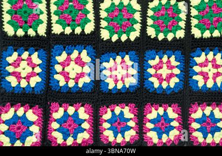 Un projet de crochet en coton vibrant avec des carrés noirs avec des centres carrés de Granny colorés en rose, blanc, bleu et vert. Banque D'Images