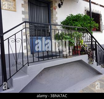 Kavala, Grèce, Un bâtiment blanc avec une porte bleue et une balustrade en fer forgé noir. La balustrade est ornée d'un panneau qui indique « Your National Dine ». Le bâtiment a une petite fenêtre de couleur sombre avec une grille décorative en métal. Une petite marche ou palier de couleur foncée est situé au bas de l'escalier. Le bâtiment est sur une rue avec un trottoir gris clair ou beige en pierre ou en béton. Plusieurs plantes en pot sont placées sur les marches et la rampe, ajoutant une touche de verdure à la scène. Un œil d'artiste et une imagination façonnée Banque D'Images
