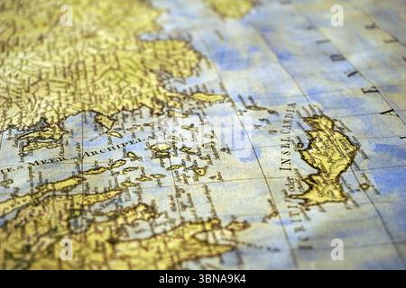 Une vue rapprochée d'une carte du monde antique, probablement du 16ème ou 17ème siècle. La carte est principalement dans les tons de jaune et de brun, avec une mer bleu-gris entourant les masses terrestres. Les masses terrestres sont représentées de manière détaillée, avec des étiquettes et des marquages indiquant les caractéristiques. La carte est orientée avec le nord en haut et comporte une grille de lignes de latitude et de longitude. Le texte sur la carte est dans une police serif, caractéristique des cartes plus anciennes. La carte est légèrement inclinée, ajoutant une sensation de perspective à la scène. La carte est le foyer central de l'image, avec l'arrière-plan légèrement flou, dr. Banque D'Images