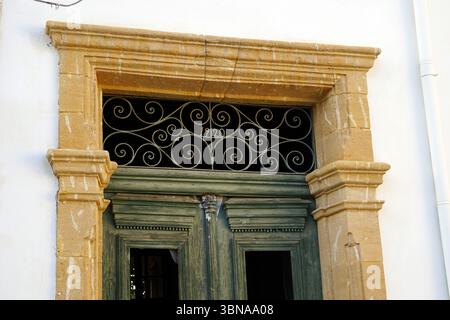 Nicosie (Lefkosia), Chypre, la dernière capitale divisée du monde, Un bâtiment blanc avec une porte en bois vert, qui est au centre de l’attention. La porte est ornée d'une grille décorative en métal avec un motif tourbillonnant et le numéro '1920' dessus. La porte est encadrée par une arche en pierre jaune, et l'extérieur du bâtiment est principalement blanc avec quelques accents de pierre beige clair ou crème. La porte a un élément décoratif sur le dessus, éventuellement une petite pièce décorative ou moulure. L'image est prise sous un angle légèrement bas, soulignant la hauteur de la porte et les détails architecturaux du Banque D'Images