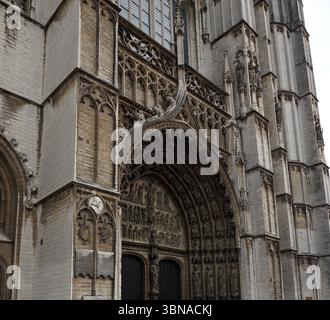La cathédrale notre-Dame. La façade de la cathédrale est principalement faite de pierre de couleur claire, avec des sculptures complexes ornant la façade. L'entrée principale présente une grande arche ornée, et la façade est décorée d'une série d'arcs plus petits et de détails. La cathédrale est sur une rue pavée, avec quelques personnes marchant au premier plan. Le ciel est couvert, et la scène globale est capturée sous un angle bas, soulignant la présence imposante de la cathédrale., Anvers, deuxième plus grande ville belge, située sur l'Escaut en Belgique. Banque D'Images