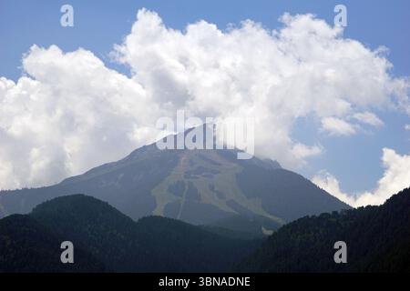 Bansko est une ville pittoresque dans le sud-ouest de la Bulgarie, nichée au pied des montagnes Pirin., Une chaîne de montagnes majestueuse sous un ciel bleu clair. La montagne, avec son sommet partiellement obscurci par une couche de nuages blancs, se dresse haute et fière. Ses pentes sont couvertes d'une végétation luxuriante et un téléski est visible sur les pistes. La chaîne de montagnes est entourée d'un mélange de montagnes vert foncé et brun/brun rougeâtre, créant un paysage diversifié. Le ciel bleu clair offre un contraste saisissant avec les teintes vertes de la montagne. Un œil d'artiste et une imagination façonnée Banque D'Images