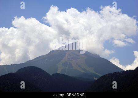 Bansko est une ville pittoresque dans le sud-ouest de la Bulgarie, nichée au pied des montagnes Pirin., Une chaîne de montagnes majestueuse sous un ciel bleu clair. La montagne, avec son pic rocheux et accidenté, est partiellement obscurcie par une épaisse couche de nuages blancs. Les pentes de la montagne sont couvertes d'une végétation luxuriante et une station de ski ou un sentier est visible à la surface de la montagne. La chaîne de montagnes est entourée de collines verdoyantes et boisées, créant une sensation de profondeur et d'échelle. Le ciel est d'un bleu clair et éclatant, et les nuages sont moelleux et blancs, ajoutant une sensation de tranquillité à la scène. An Banque D'Images