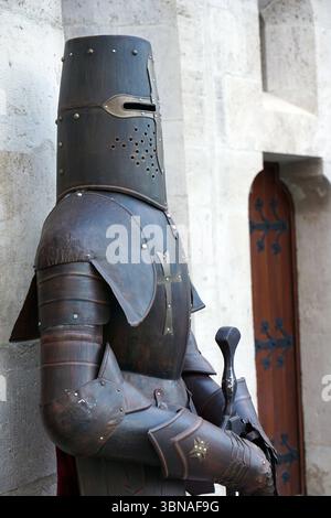 Budapest, Hongrie – la perle enchanteresse du Danube., colline du château de Budapest. Un chevalier en pleine armure debout devant un mur de pierre. L'armure du chevalier est principalement brun foncé ou noir, avec des accents dorés sur le casque, la plaque de poitrine et d'autres détails. Le chevalier tient une épée dans sa main droite. Le casque du chevalier présente un grand corps cylindrique avec une petite ouverture en haut, et une croix est affichée en évidence sur la plaque de poitrine. L'armure du chevalier comprend également des plaques d'épaule et d'autres détails. Le mur de pierre derrière le chevalier est fait de pierre de couleur claire et d'un bois Banque D'Images