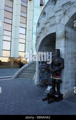 Budapest, Hongrie – la perle enchanteresse du Danube., Statue de l'Étienne Ier, Bastion des pêcheurs, colline du château de Budapest. Une arche en pierre, partie d'un bâtiment plus grand, avec une statue de chevalier debout de garde sur le côté droit. La statue est habillée d'un costume brun foncé/noir avec des accents rouges et un casque, et elle est positionnée sur un petit support en bois. Un panneau sur le stand indique « ne touchez pas l'armure du chevalier ». À gauche de l'arche, un ensemble d'escaliers mène à un bâtiment moderne avec de grandes fenêtres. La façade du bâtiment est principalement blanche avec quelques accents bleus. Le sol devant le Banque D'Images