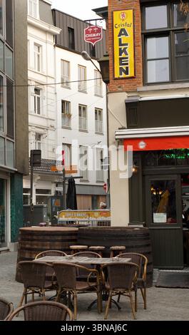 Anvers, deuxième plus grande ville belge, située sur l'Escaut en Belgique., Une rue pavée pittoresque, bordée de bâtiments dans les tons de blanc, gris et beige. La rue est ornée de coins salon extérieurs, y compris des tables et des chaises, et quelques personnes sont visibles en arrière-plan. Un pub nommé « cristal Alken » est bien en évidence sur le côté droit de l'image, avec un auvent rouge et un panneau indiquant qu'il s'agit d'un établissement « Chimay ». Un grand tonneau en bois est situé en face du pub. Les bâtiments en arrière-plan sont à plusieurs étages et présentent un mélange de styles architecturaux, Banque D'Images