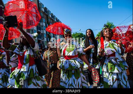 Amsterdam, pays-Bas. 01 juillet 2025. On voit des femmes surinamaises danser avec des parapluies rouges. Le 1er juillet 1863 marque la fin de l’esclavage pour les Surinamais. Ce défilé fait partie du festival 'Keti Koti' ('chaînes brisées' en Surinamais), qui est ouvert par un défilé coloré en vêtements traditionnels appelé Bigi Spikri. Crédit : SOPA images Limited/Alamy Live News Banque D'Images