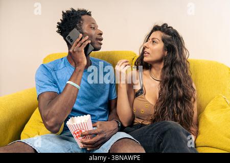Un homme parle sur son téléphone portable, ignorant sa petite amie agacée assise à côté de lui sur le canapé. Banque D'Images