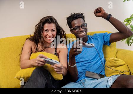 Un jeune couple excité fête après avoir gagné un jeu vidéo, joué ensemble sur un canapé à la maison et se sentant triomphant. Banque D'Images
