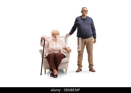 Homme mûr debout à côté d'une femme âgée assise dans un fauteuil isolé sur fond blanc Banque D'Images