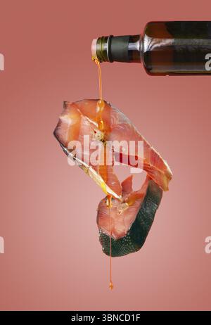 L'huile d'olive est versée sur des morceaux de saumon rose, sur un fond rose, nourriture volante Banque D'Images