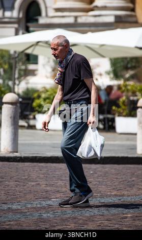Homme senior portant un Jean t-shirt noir et un sac banane transportant des courses. Banque D'Images
