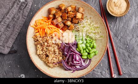 Bol de quinoa coloré avec edamame, tofu, chou rouge et carottes - un repas équilibré et riche en protéines à base de plantes servi avec des baguettes sur le côté. Banque D'Images