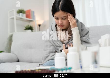 Jeune femme asiatique ayant une forte fièvre tout en vérifiant la température corporelle, les éternuements féminins et le nez qui coule avec la grippe saisonnière, la prise de médicaments, virus, c Banque D'Images