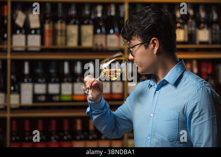 Expert professionnel du vin évaluant l'arôme du vin blanc dans le verre avec fond d'étagère de vin flou Banque D'Images