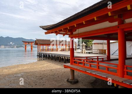 Le sanctuaire sacré Itsukushima avec sa porte torii rouge flottante surplombe les eaux calmes et les montagnes de l'île de Miyajima au Japon Banque D'Images