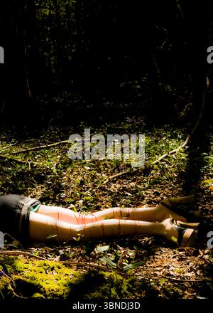 Une personne est allongée sur le sol de la forêt, ses jambes et ses pieds visibles. Du sang est visible sur leurs jambes. Banque D'Images