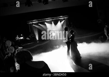 Un couple silhouette partage une danse romantique sur une scène, entouré de faisceaux de projecteurs spectaculaires et de fumée atmosphérique, dans un noir et blanc intemporel Banque D'Images